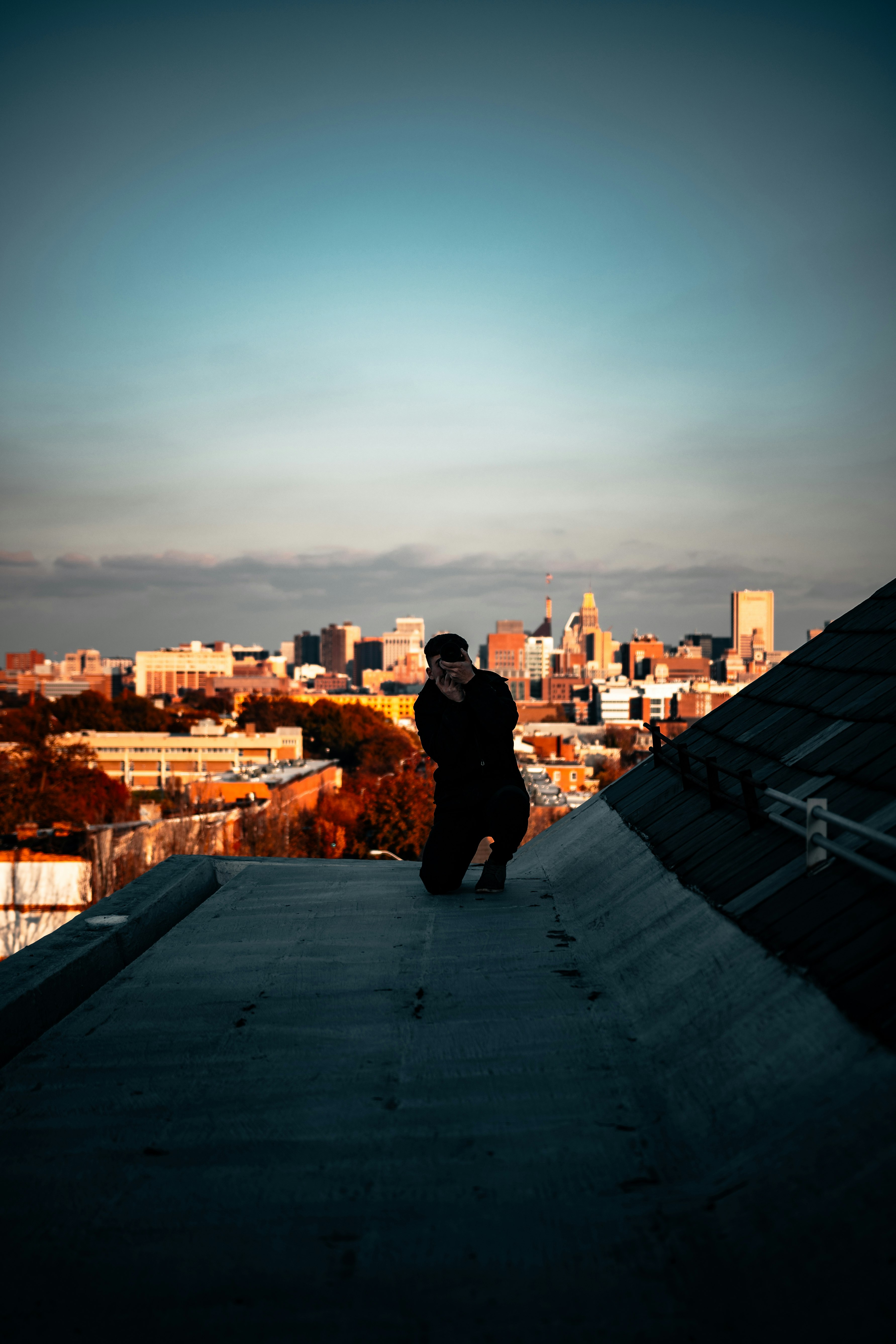 man in black jacket sitting on roof top looking at city buildings during daytime